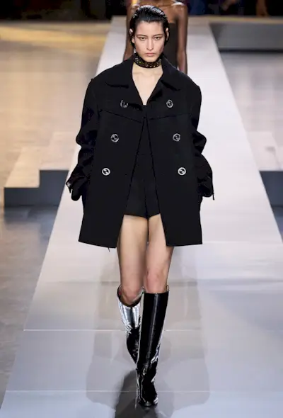 best riding boots shown in a photo from Gucci's fall 2024 runway show with a model wearing a black peacoat with a black top, hot pants, and black riding boots
