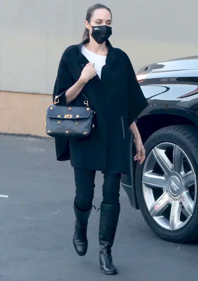 the best riding boots shown in a photo of Angelina Jolie wearing a black cape over a white t-shirt with black skinny jeans and black knee-high riding boots