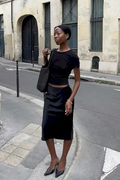 a photo showing what shoes to wear with skirts with a woman standing in the street wearing a black t-shirt with a black satin midi skirt with black kitten pointed pumps