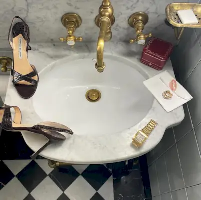 A flat lay on a marble sink featuring Manolo Blahnik heels and a gold Cartier Tank watch.