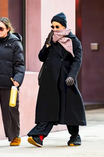 Jennifer Lawrence wears a black beanie, sunglasses, red scarf, black jacket, black Loewe sneakers, and red socks.