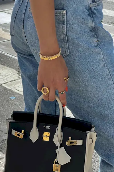 Cass Dimicco wearing jeans, a Hermes bag, gold rings, and gold bracelets.