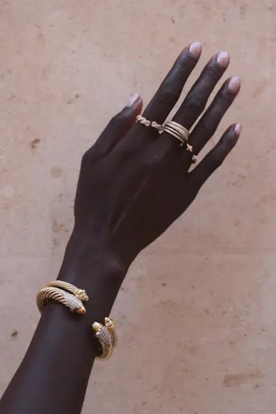 A woman's arm that shows gold rings and two gold bracelets.