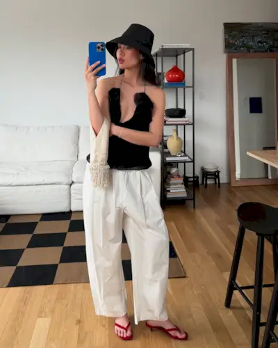 Influencer Mimi wears white barrel, an black floral top a black hat and takes photo with a blue iphone.