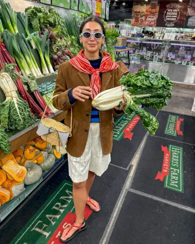 Influencer Barbra wears linen shorts, stripped jumper a brown blazer and holds a wicker bag.