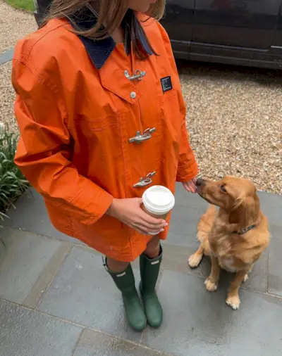 Paige wears an orange jacket and green rain boots.