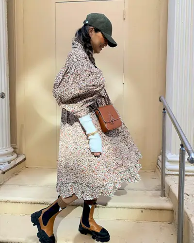 Caroline wears a floral maxi dress, tan lug-sole boots, a JW anderson tan crossbody bag, white gloves, and a green baseball cap.