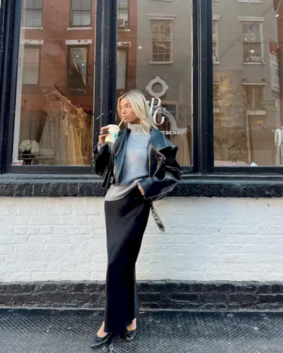 Kit wears a black leather jacket, gray turtleneck sweater, black maxi slip skirt, and black ballet flats.