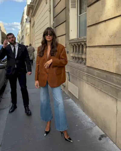 Influencer @juliesfi wears a brown suede blazer with blue flares jeans and black heels.