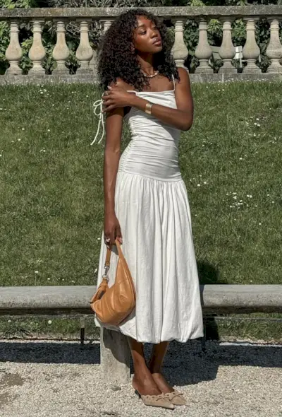 @emmanuellek_ wears a white midi bubble-hem dress with light brown mules and a tan suede bag
