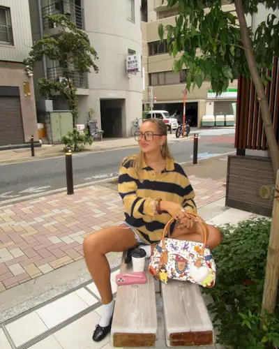 Influencer isabellapmayer in a beige and black striped polo, blue denim shorts white socks and black ballet flats.