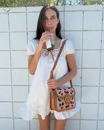 Influencer devonleecarlson in a white babydoll dress with a red trim carrying a Valentino wicker bag.