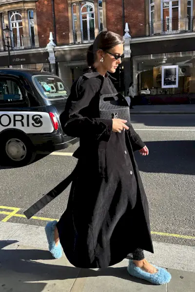 a photo showing how to wear dresses in the winter with a woman wearing a black long trench coat over a sequin maxi dress with furry flats