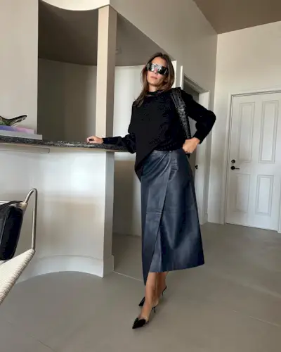 Jen Wonders in a black sweater, leather wrap skirt, and black heels.