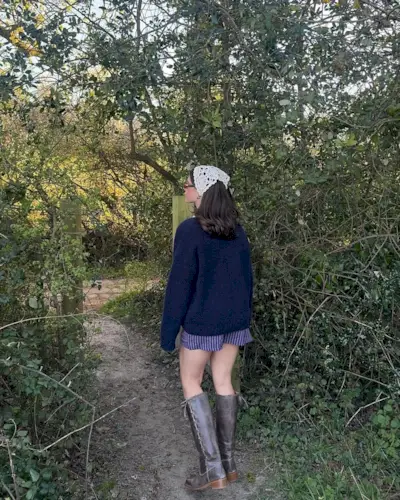 A woman standing wearing stripped boxer shorts, a blue sweater, and laced-up grey boots.