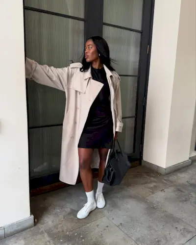 @nlmarilyn wears white trainers with a black mini dress and cream trench coat