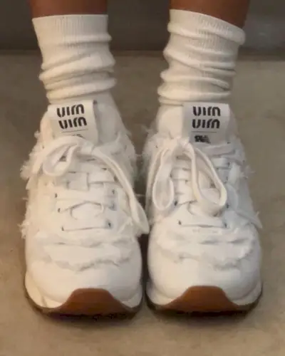 A woman wears miu miu x new balance sneakers in white with tube socks.