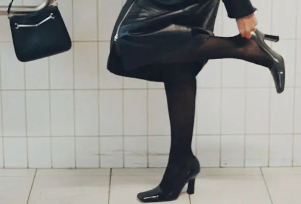 Hanna MW wearing a leather skirt suit with tights and block-heel pumps.