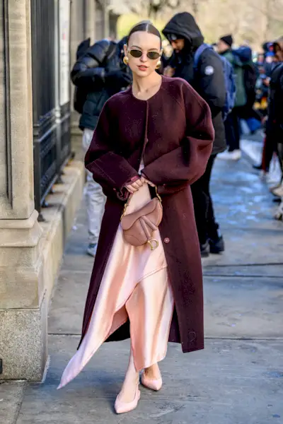 Woman wearing a powder pink dress and burgundy coat.