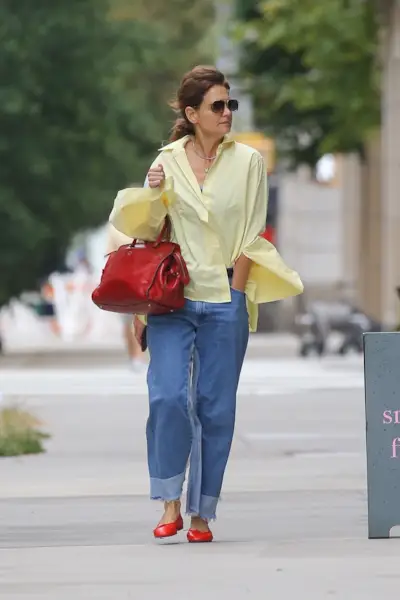 Katie Holmes wearing a yellow button-down, blue jeans, and a red bag and flats
