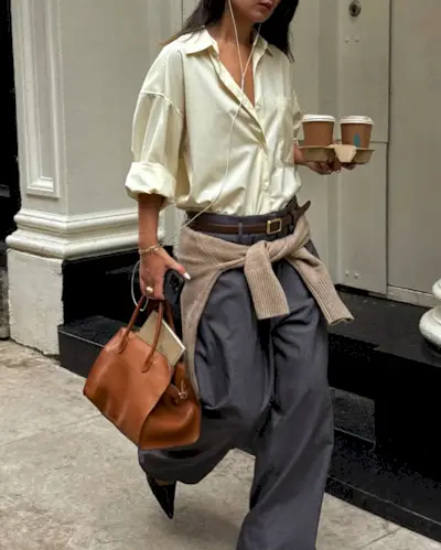 @thecarolinelin wears a pair of grey trousers and a butter yellow shirt with a tan jumper around the waist