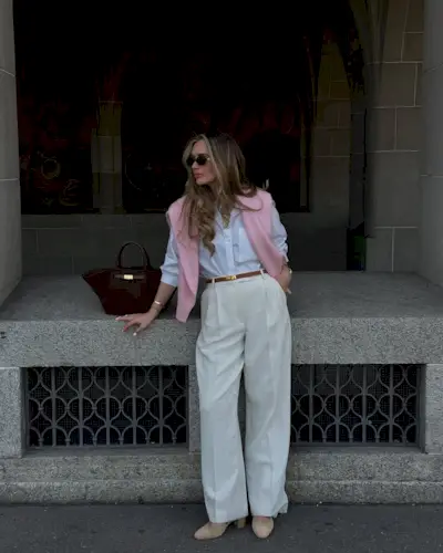 @oliviafaeh wears a pink jumper around her shoulders, a white shirt and cream trousers