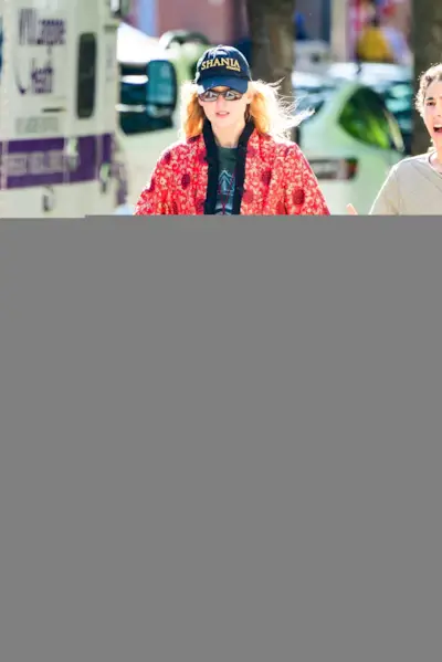 Jennifer Lawrence wears a red jacket, baseball cap, black pants, and ballet sneakers.