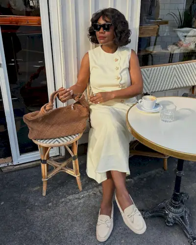 Influencer @frannfyne sits outside of a cafe in Paris wearing a cream two-piece and suede boat shoes.