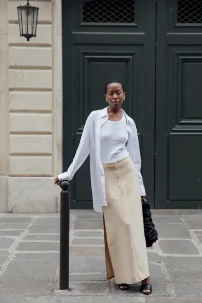 a photo showcasing one of the best summer work outfits with a woman wearing a white oversize button down shirt over a white tank with a maxi pencil skirt and black mules