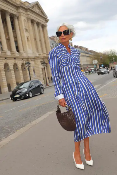 a photo showcasing one of the best summer work outfits with a woman wearing a blue stripped button-down shirt dress with white pumps and a brown handbag