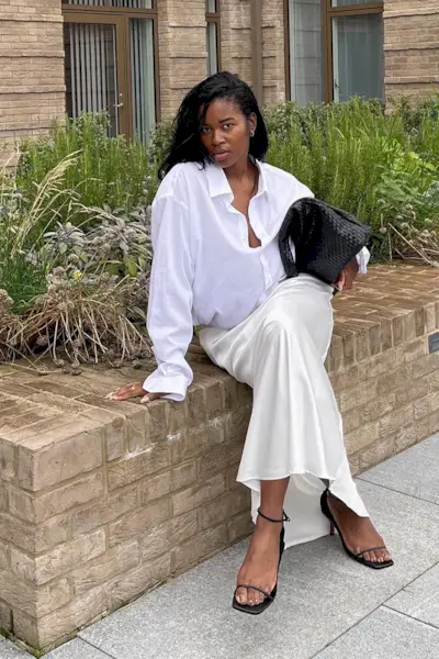 a photo showcasing one of the best summer work outfits with a woman wearing a white button-down shirt with a white slip maxi skirt and black sandals