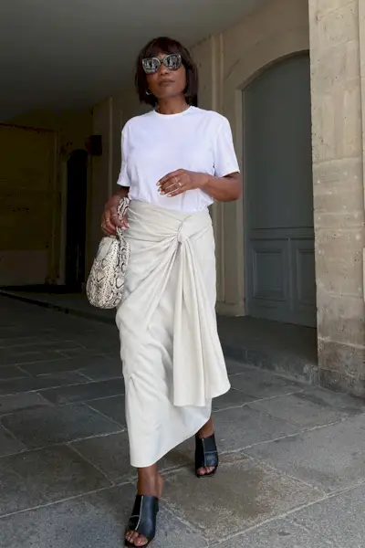 a photo showcasing one of the best summer work outfits with a woman wearing a white t-shirt with a tan wrap skirt with a snakeskin bag and black mules