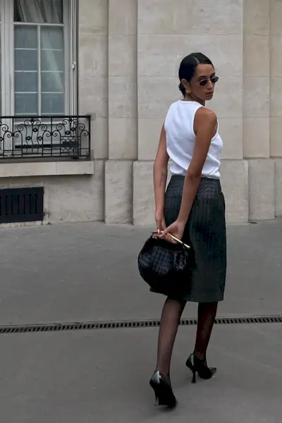 a photo showcasing one of the best summer work outfits with a woman wearing a white tank top with a pencil skirt, tights, black pointed pumps, and a Bottega Veneta handbag