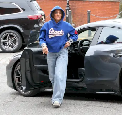 Jennifer Lopez wears a blue Giants sweatshirt, light-wash wide-leg jeans, and white sneakers.