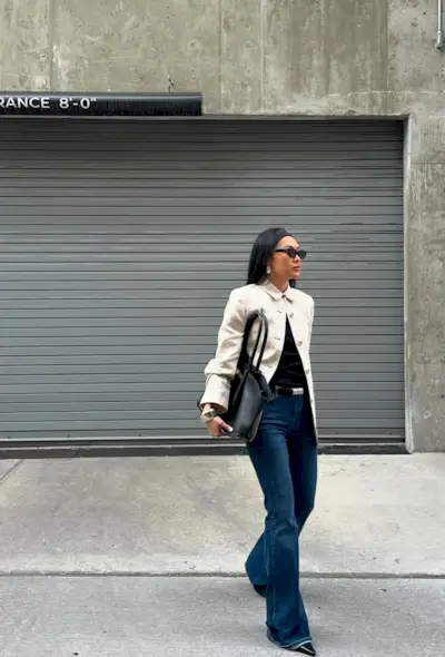 a photo showing what shoes to wear with wide-leg pants with a woman wearing a white coat over a black top with wide-leg jeans and black pointed-ankle boots