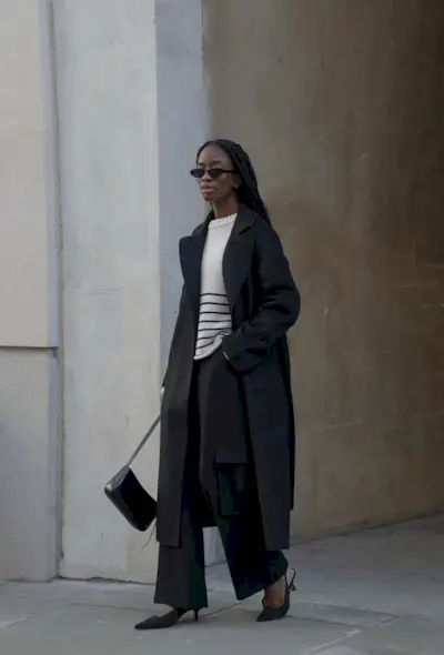 a photo showing what shoes to wear with wide-leg pants with a woman wearing a black trench coat over a black and white striped sweater styled with black wide-leg pants and black slingback heels