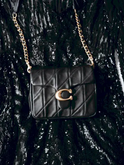 A black Coach flap crossbody bag with a gold chain.