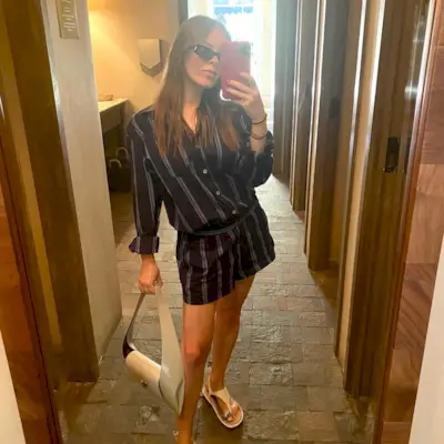 Nikki wears a stripe romper, white sandals, and a gray handbag.