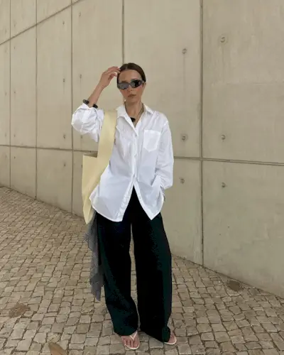 Debora wears a white button-down shirt, black pants, and white flip-flops.