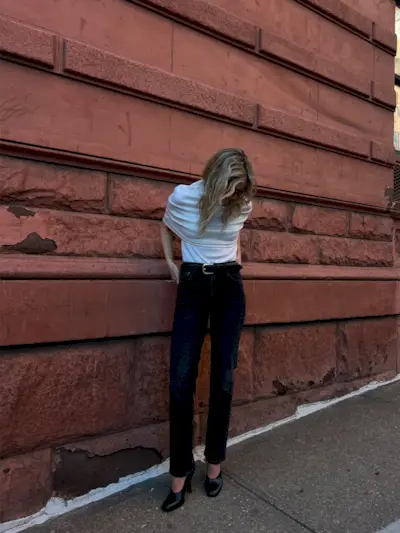 Eliza Huber wearing a cream knit top, a black belt, black Citizens of Humanity Zurie jeans, and black shoes.