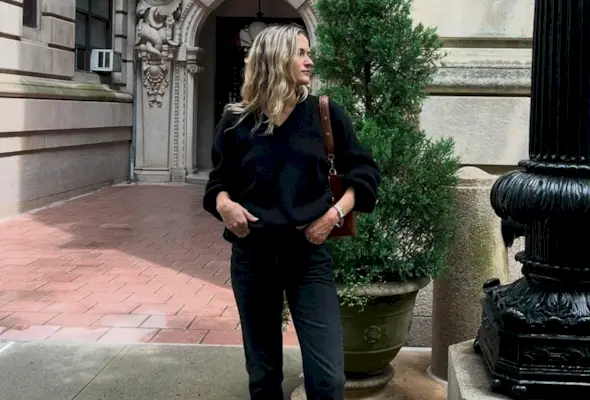 Eliza Huber wearing a black V-neck sweater, brown bag, black Citizens of Humanity Zurie black jeans, and brown shoes.