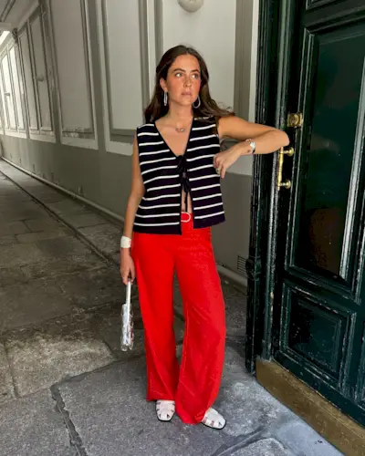 Alex is wearing red pants, white fisherman flats, a silver handbag, and a striped knit top.