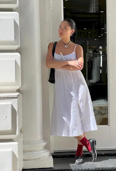 A woman's white dress outfit idea with a spaghetti strap dress styled with red socks and black loafers.
