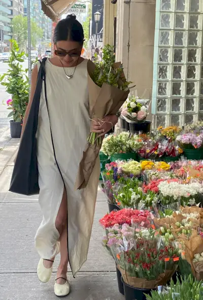A woman's white dress outfit with long maxi styled with a silver necklace, white ballet flats, and a black tote bag.