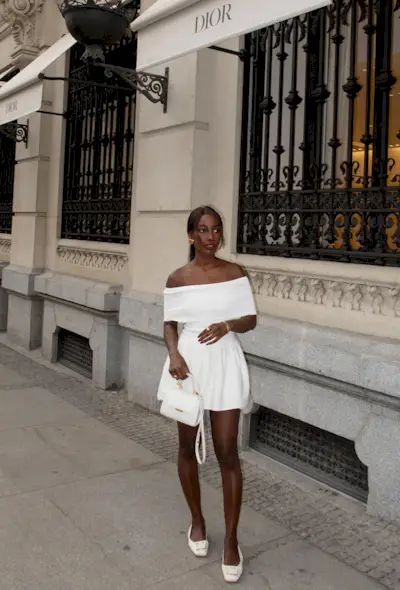 A woman's white dress outfit styled with white slingbacks, a white handbag, and gold earrings.