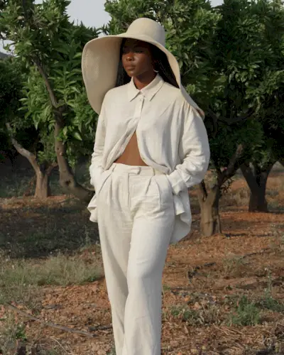 Woman wearing a white linen outfit and oversize hat.