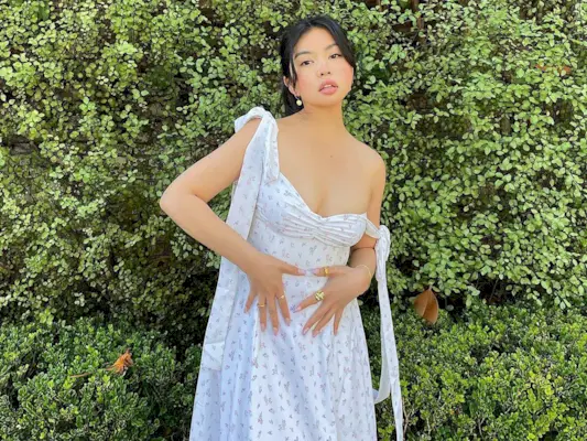 Woman standing in front of a hedge wearing a white floral print dress.